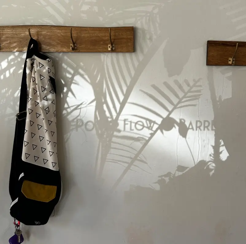 A mat bag on a wooden hook with Power Flow and Barre lettered on the studio wall